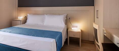 Ein ordentlich bezogenes Bett mit blauer und weißer Bettdecke, zwei Nachttische mit Lampen und ein Holzschrank.