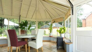 A covered patio with a table and chairs, potted plants, and a birdcage. - Bournes Farmhouse (Henley-on-Thames)