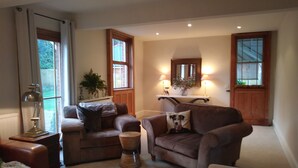 A cozy living room with two sofas, a coffee table, and a lamp. There are windows with curtains, a mirror, and a small plant on a shelf. - Bournes Farmhouse (Henley-on-Thames)
