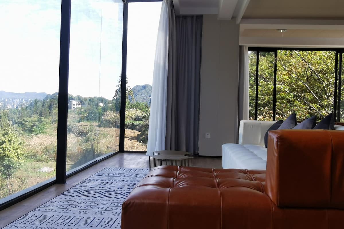 A modern living room with a large window, a brown leather sofa, and a white couch.