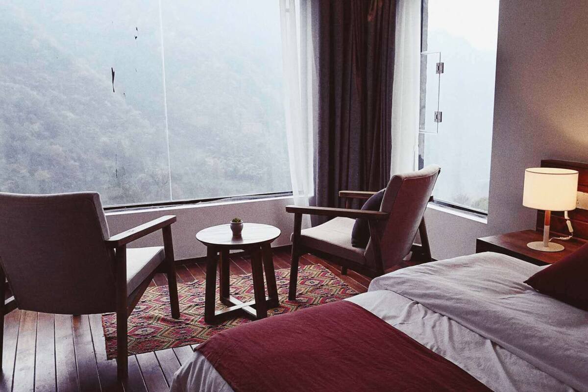 A hotel room with a bed, two armchairs, a small table, a lamp, and a view of the outdoors.