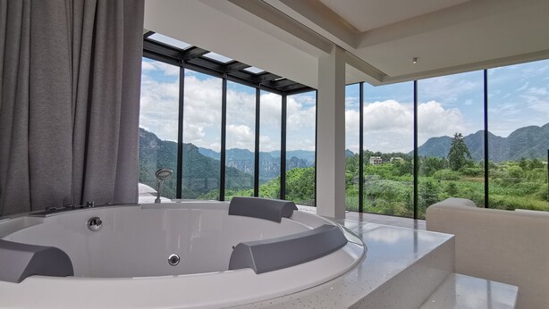 A modern bathroom with a large bathtub, a shower, and a view of mountains through large windows. - Purespace (Zhangjiajie)