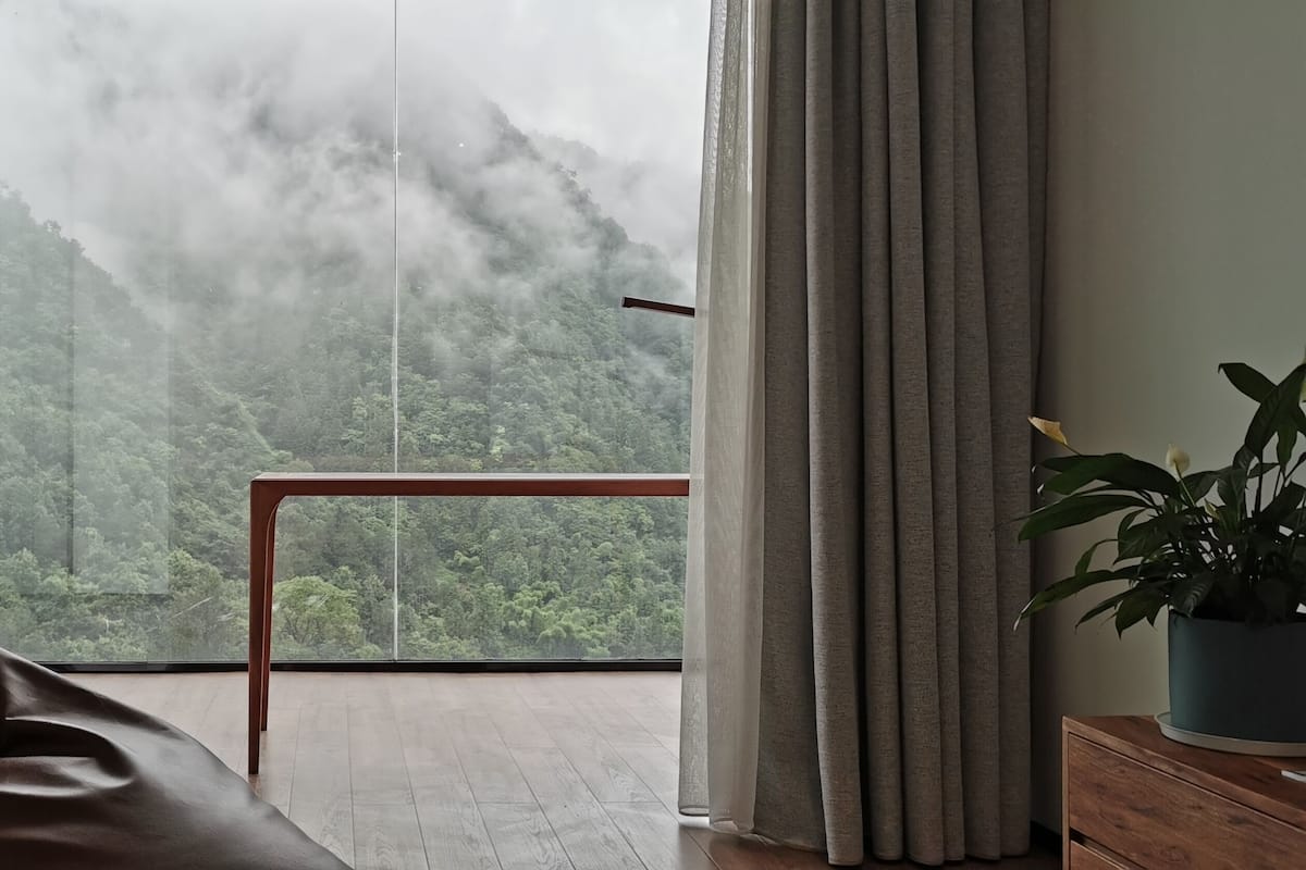 A room with a large window, a wooden table, a sofa, and a potted plant.