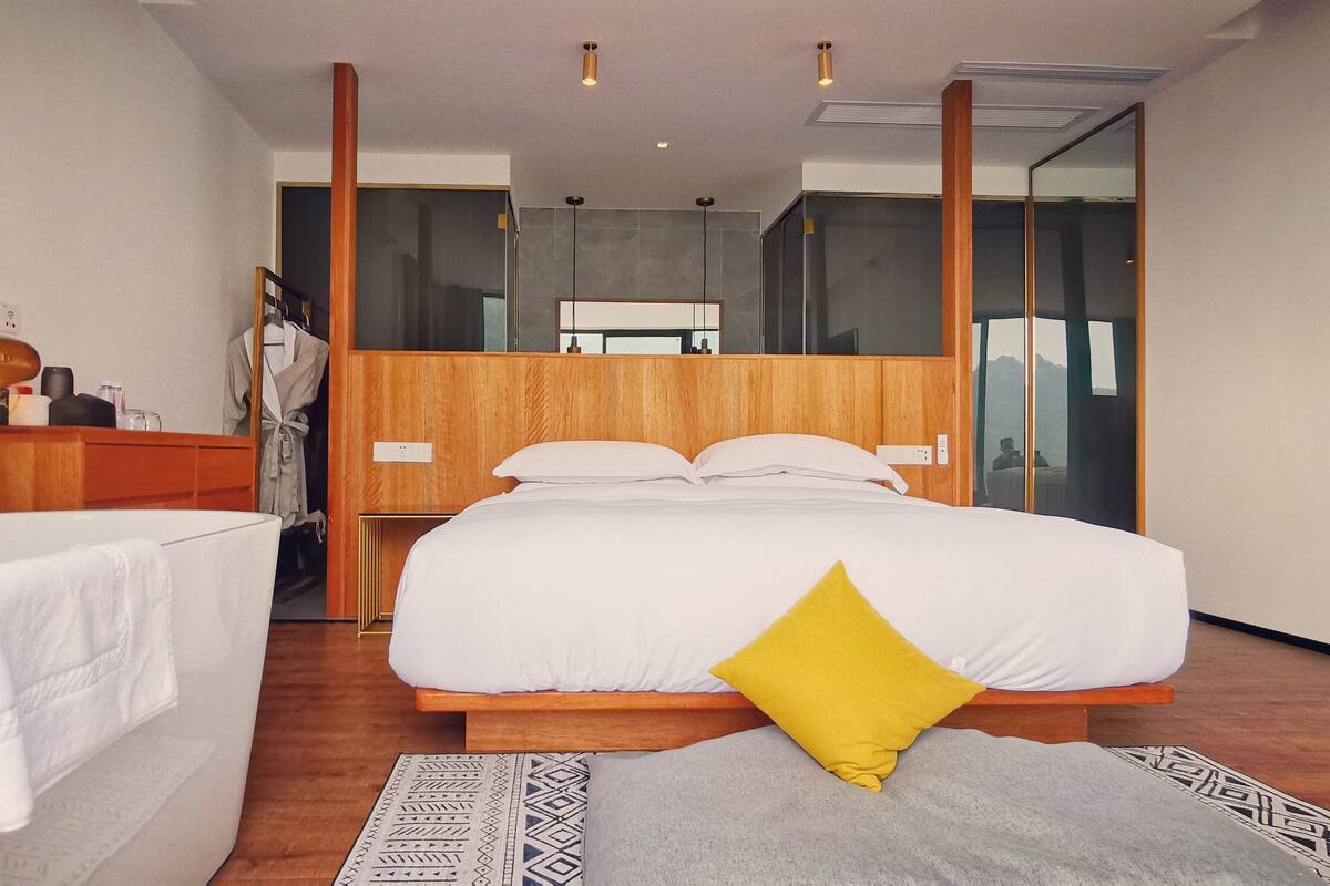 A modern hotel room with a large bed, a separate bathroom, a wooden wardrobe, and a mirror.