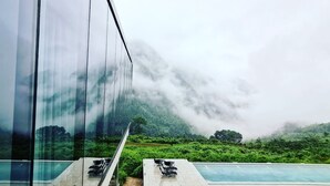 A modern building with a glass facade overlooking a lush green landscape and a pool area. - Purespace (Zhangjiajie)