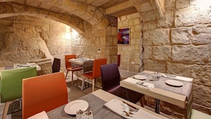 A restaurant with stone walls and arched ceilings, featuring tables and chairs in various colors. - Palazzo Paolina Boutique Hotel (Valletta)
