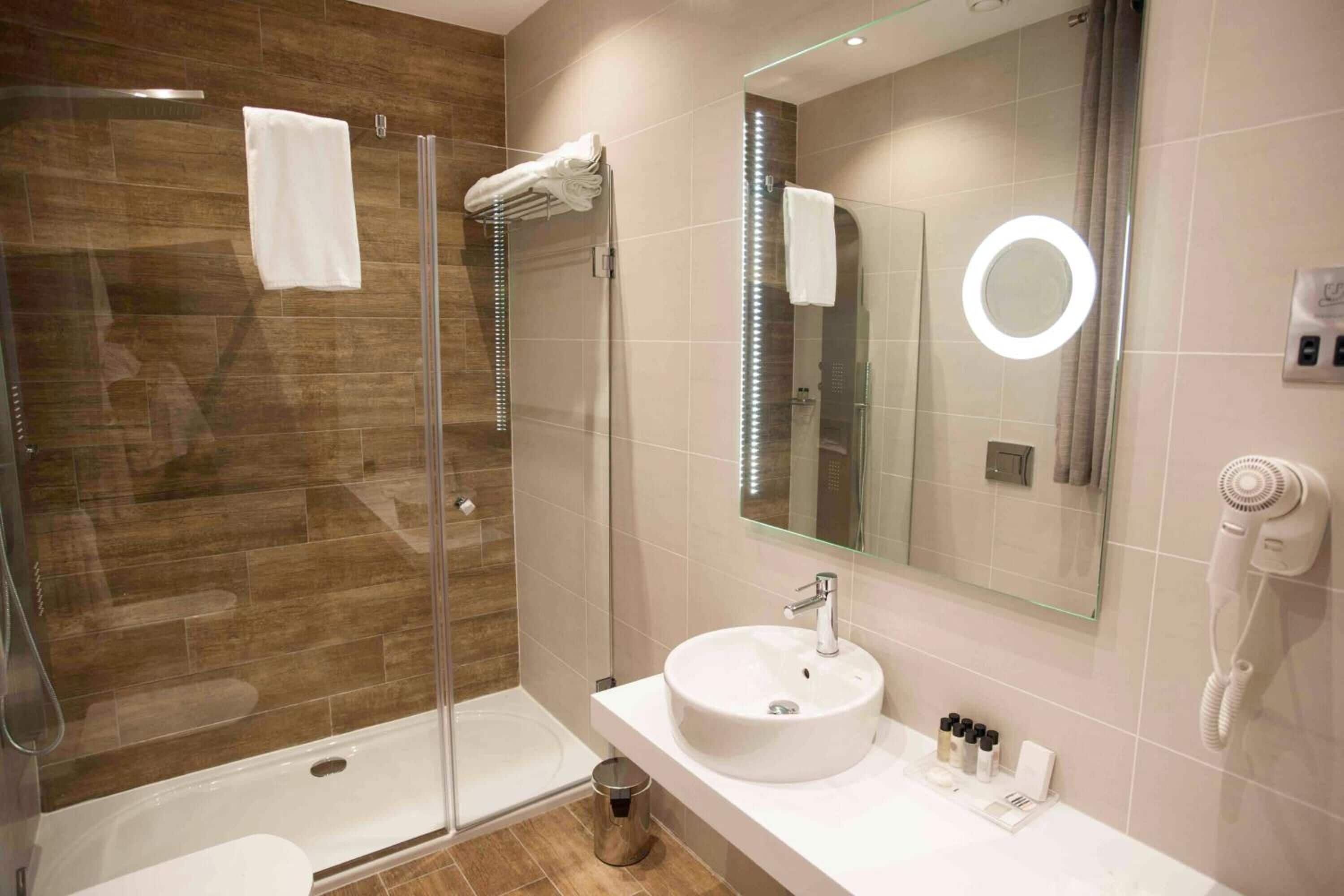 A modern bathroom with a glass-enclosed shower, a white sink, and a large mirror.