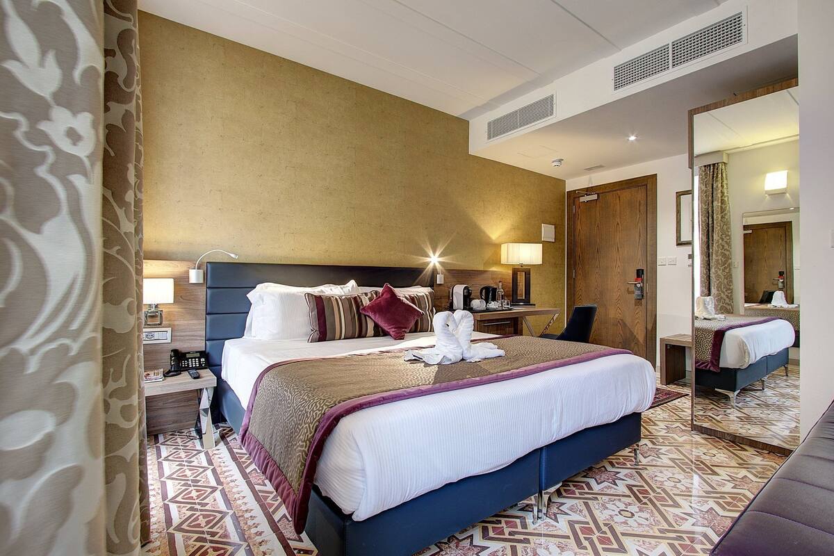 A hotel room with a large bed, bedside tables, a mirror, and a patterned floor.