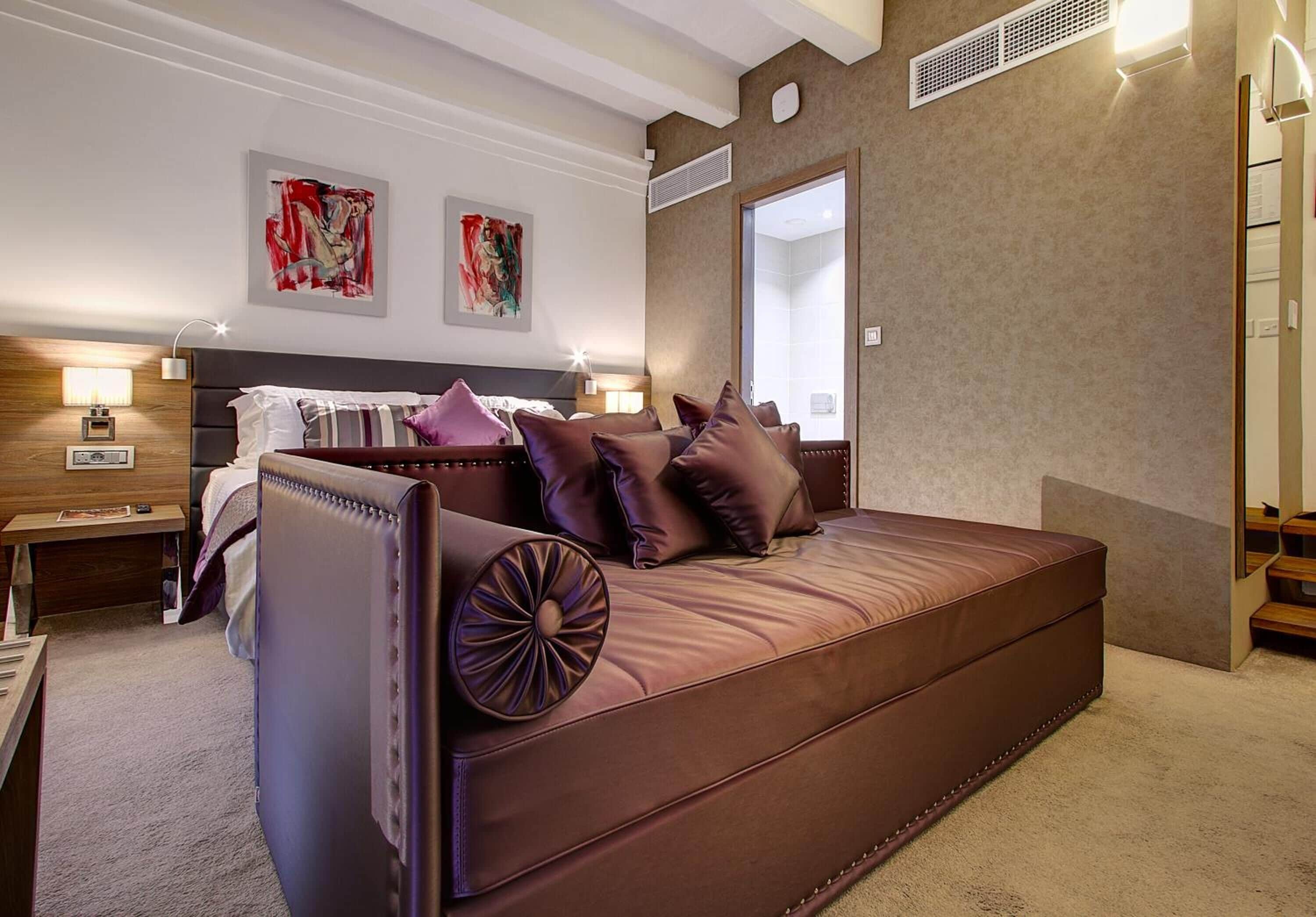 Quarto de hotel moderno com cama grande, mesa de cabeceira, espelho fixado na parede e obras de arte nas paredes.