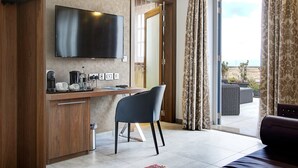 A modern hotel room with a flat-screen TV, a wooden desk with a chair, a balcony with outdoor furniture, and a sliding glass door. - Palazzo Paolina Boutique Hotel (Valletta)