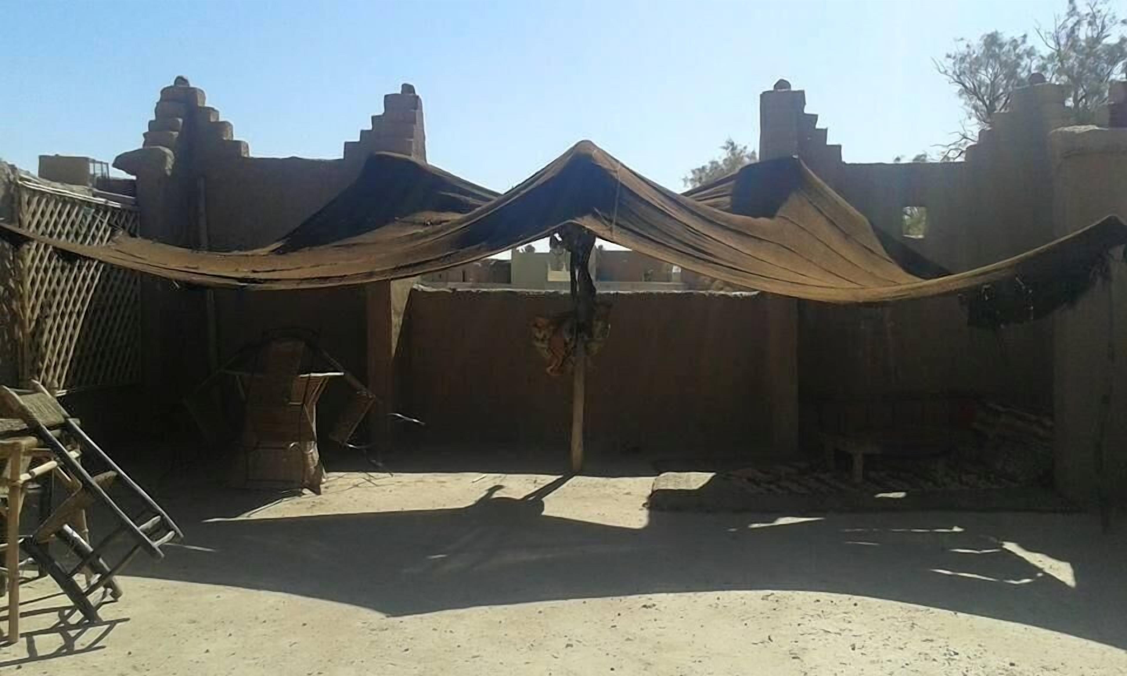 A courtyard with a large tent-like structure, a wooden ladder, and a brick wall.