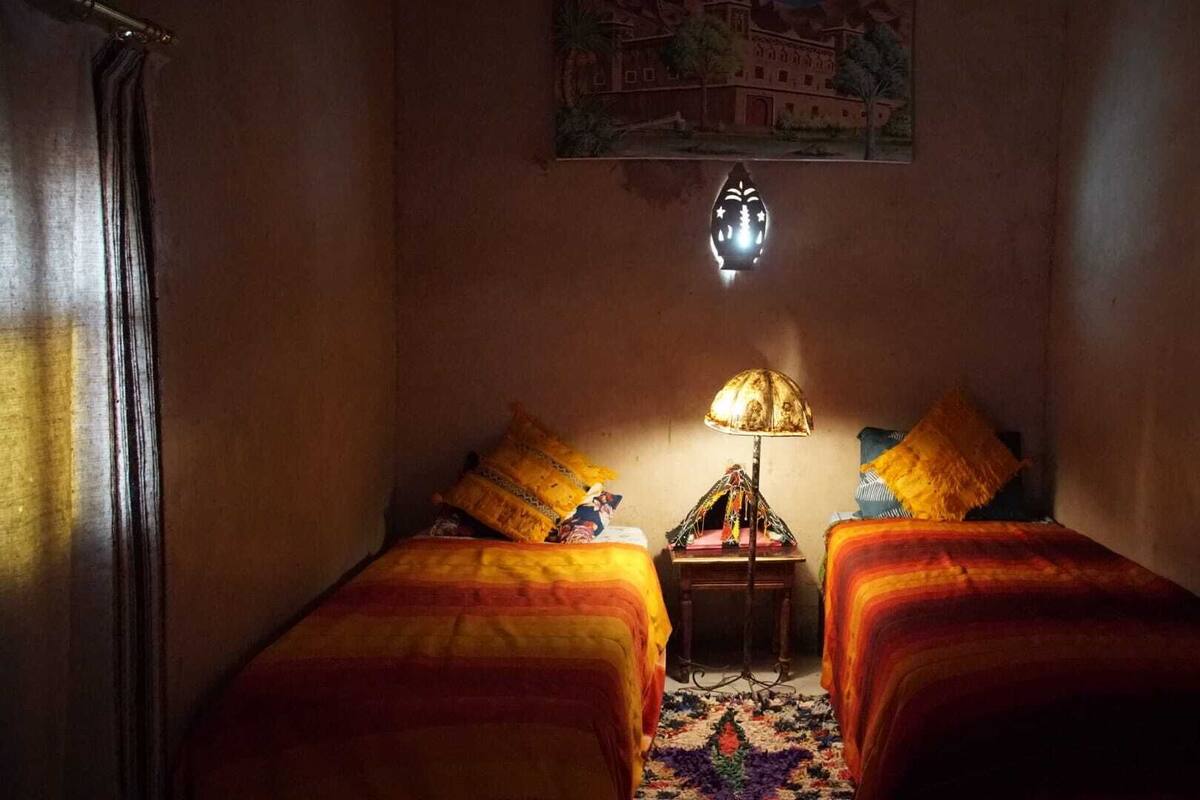 Una habitación con dos camas, una mesita de noche, una lámpara y un aplique de pared.