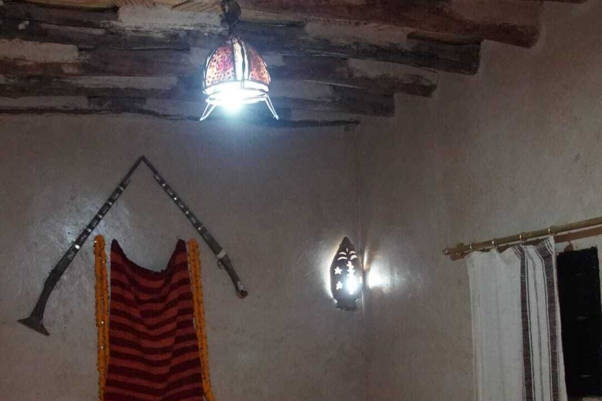 Una habitación con cama, lámpara colgante, luz en la pared y ventana con cortinas.