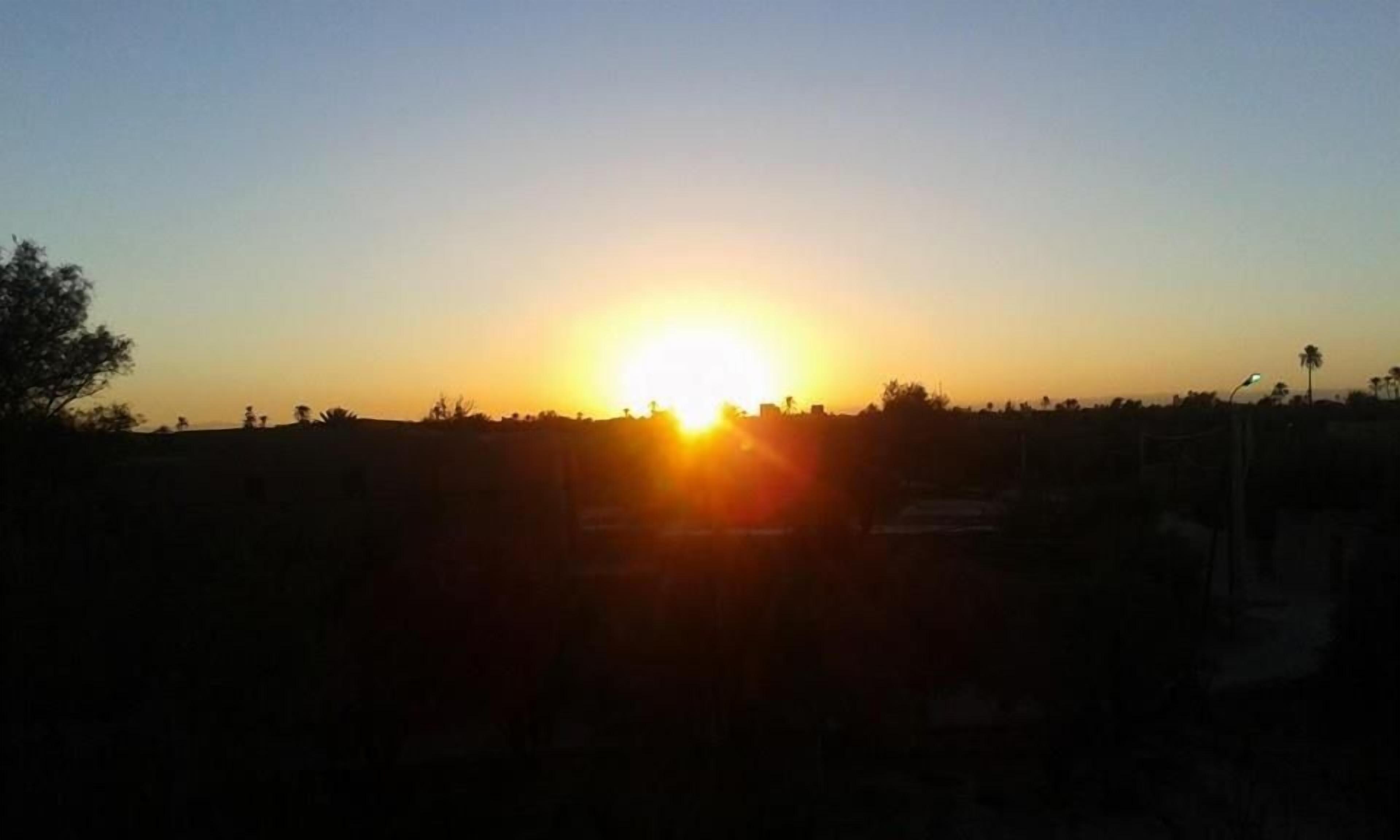 A sunset over a flat landscape with silhouettes of trees and a distant horizon.