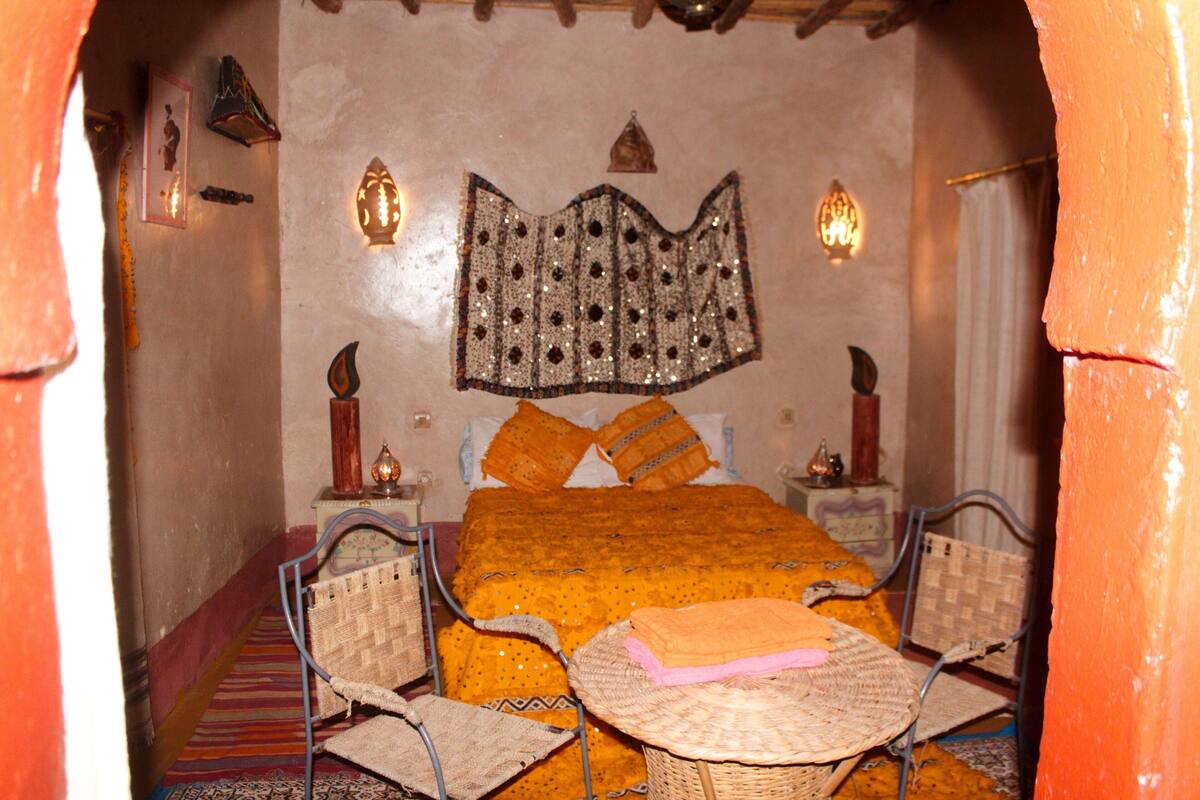Una habitación tradicional con una cama, dos sillas, una mesita y adornos en las paredes.