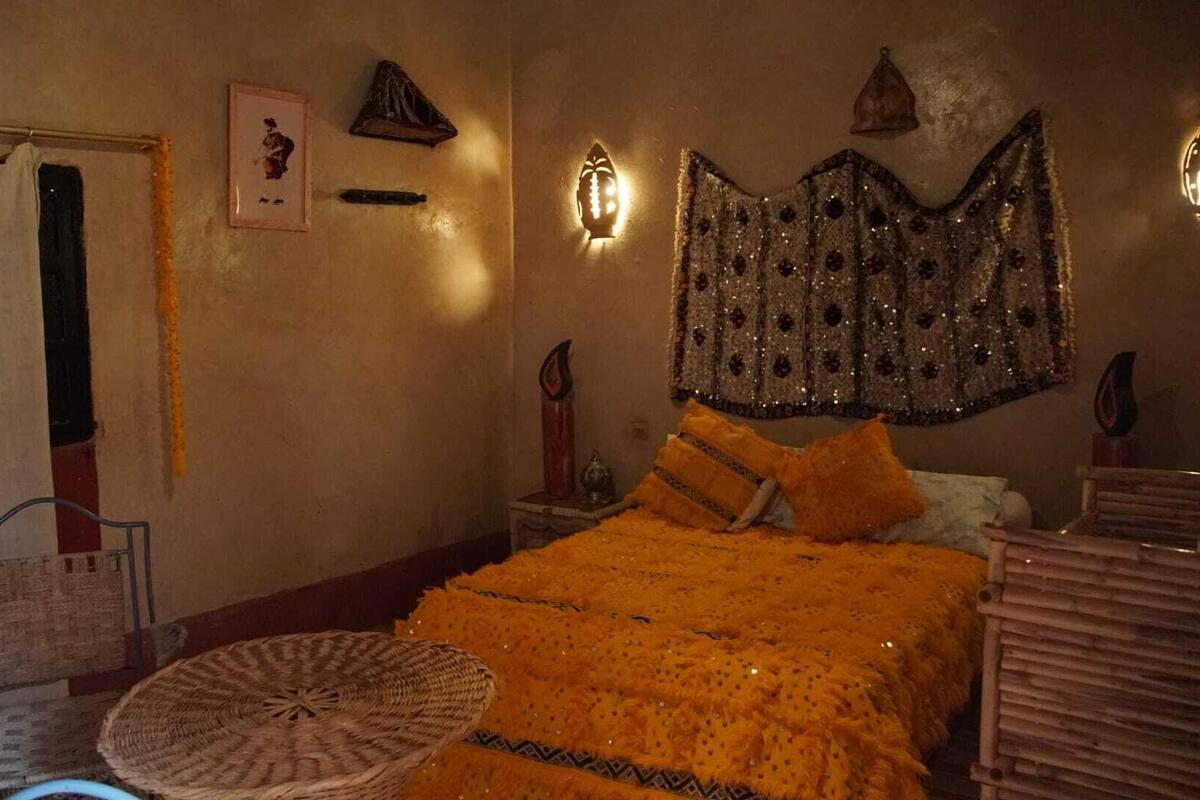 Una habitación con cama, una silla, un tapiz y una mesita.