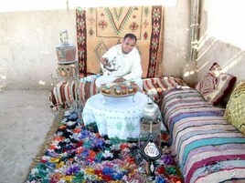 Una habitación con una cama con diseño, una mesita redonda con una tetera y una alfombra colorida.
