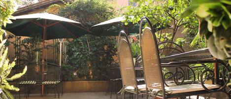 Outdoor seating with metal chairs and tables, surrounded by greenery and umbrellas.
