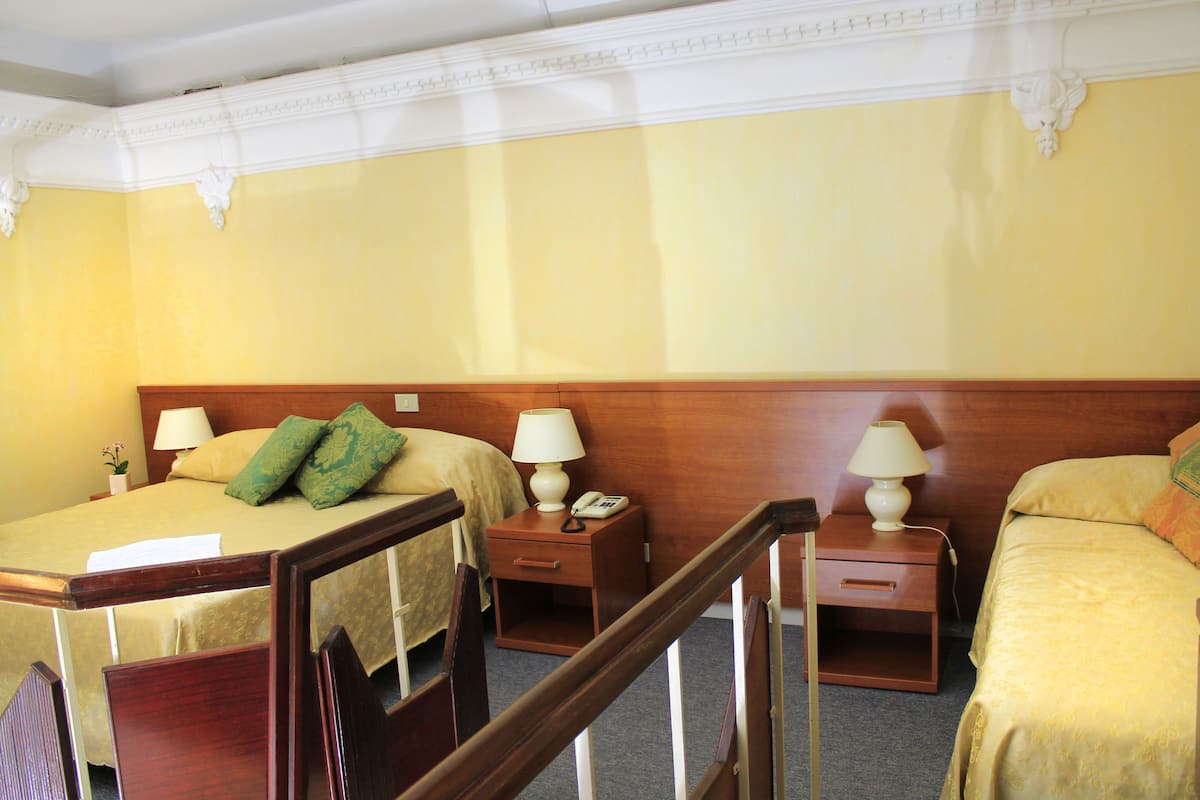 Une chambre d’hôtel avec deux lits, une tête de lit en bois, des tables de chevet avec des lampes et une petite table de nuit.