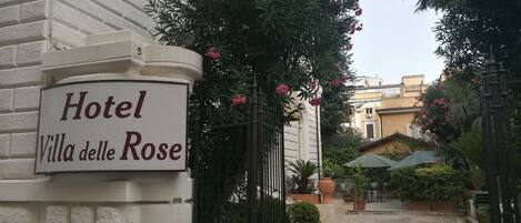 Un letrero del Hotel Villa delle Rose con un camino pavimentado que lleva a una reja.