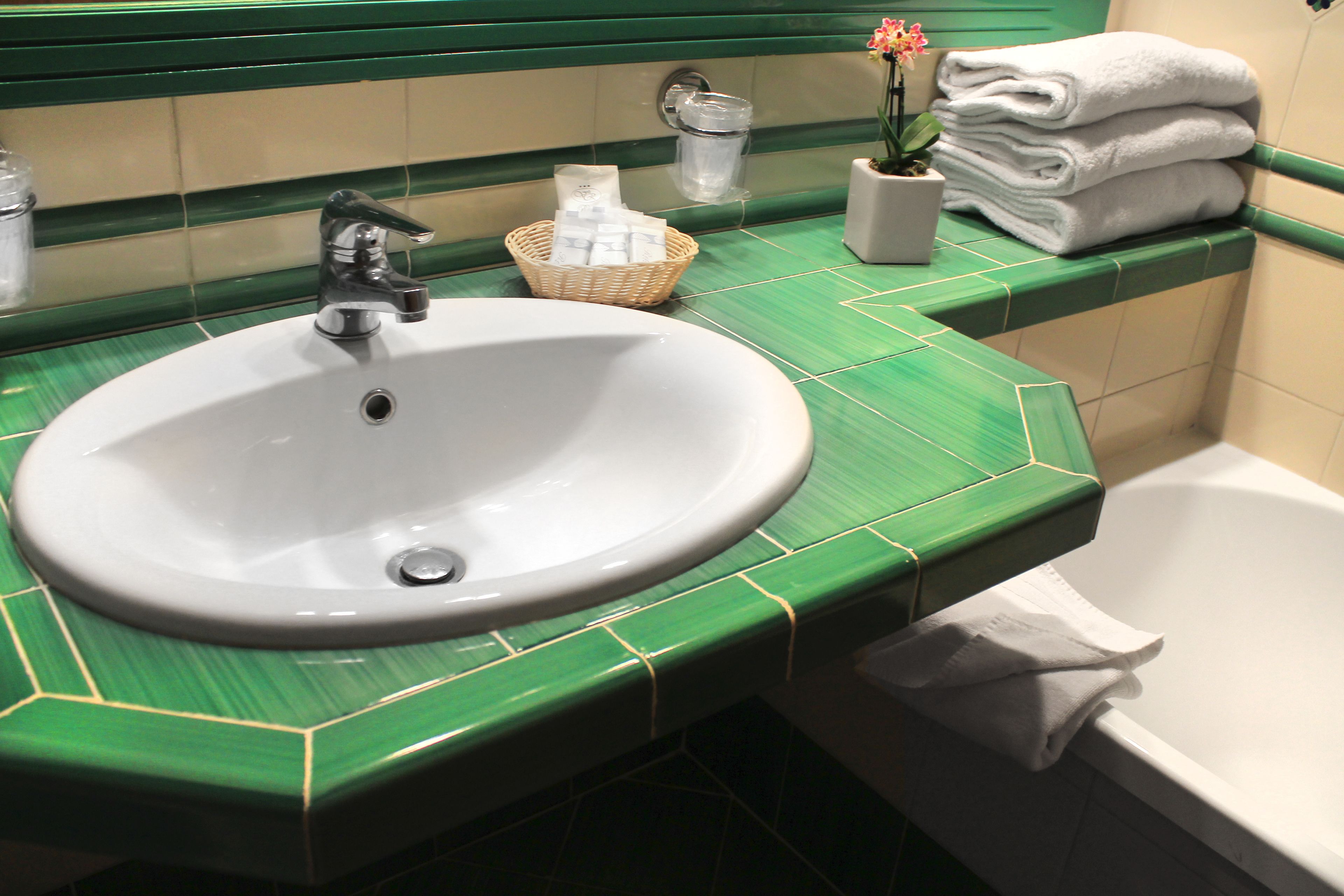 Un baño con un lavabo blanco, encimera con azulejos verdes y una bañera blanca.