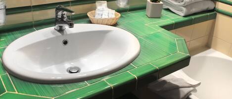 Un baño con un lavabo blanco, encimera con azulejos verdes y una bañera blanca.