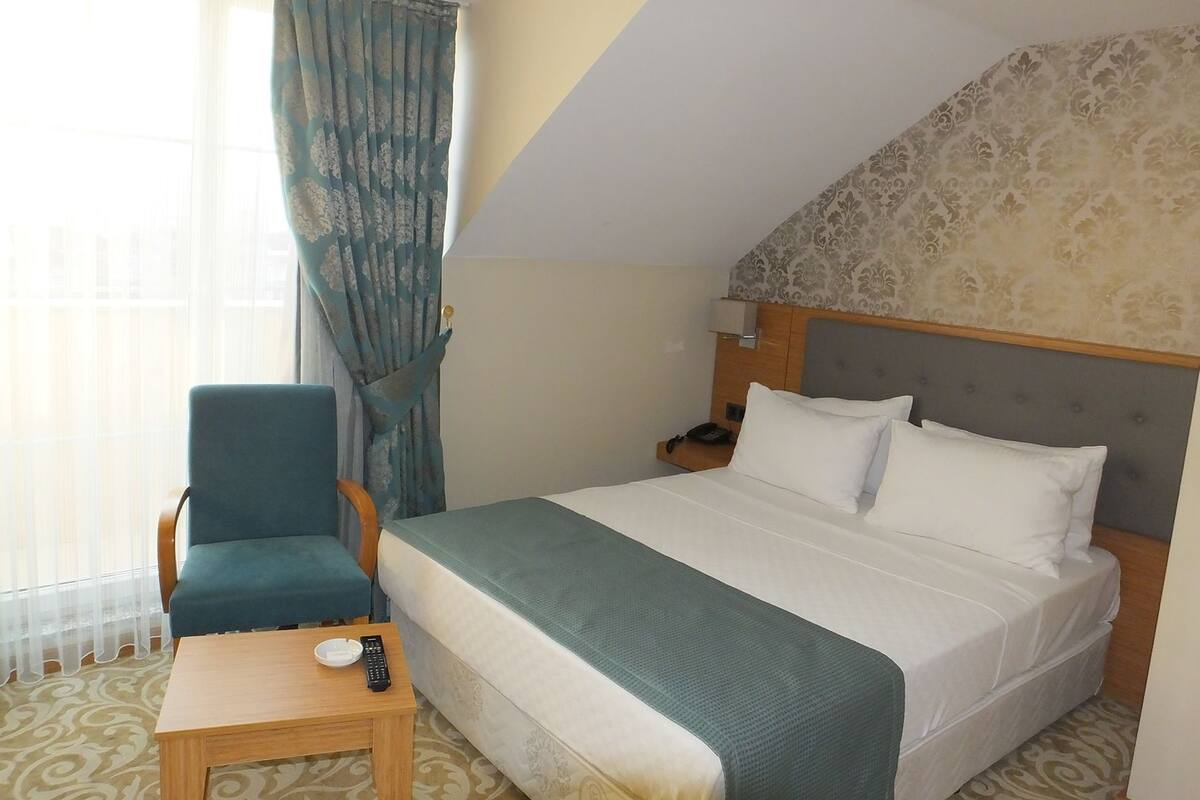 A hotel room with a bed, a chair, a small table, a lamp, and a window with curtains.