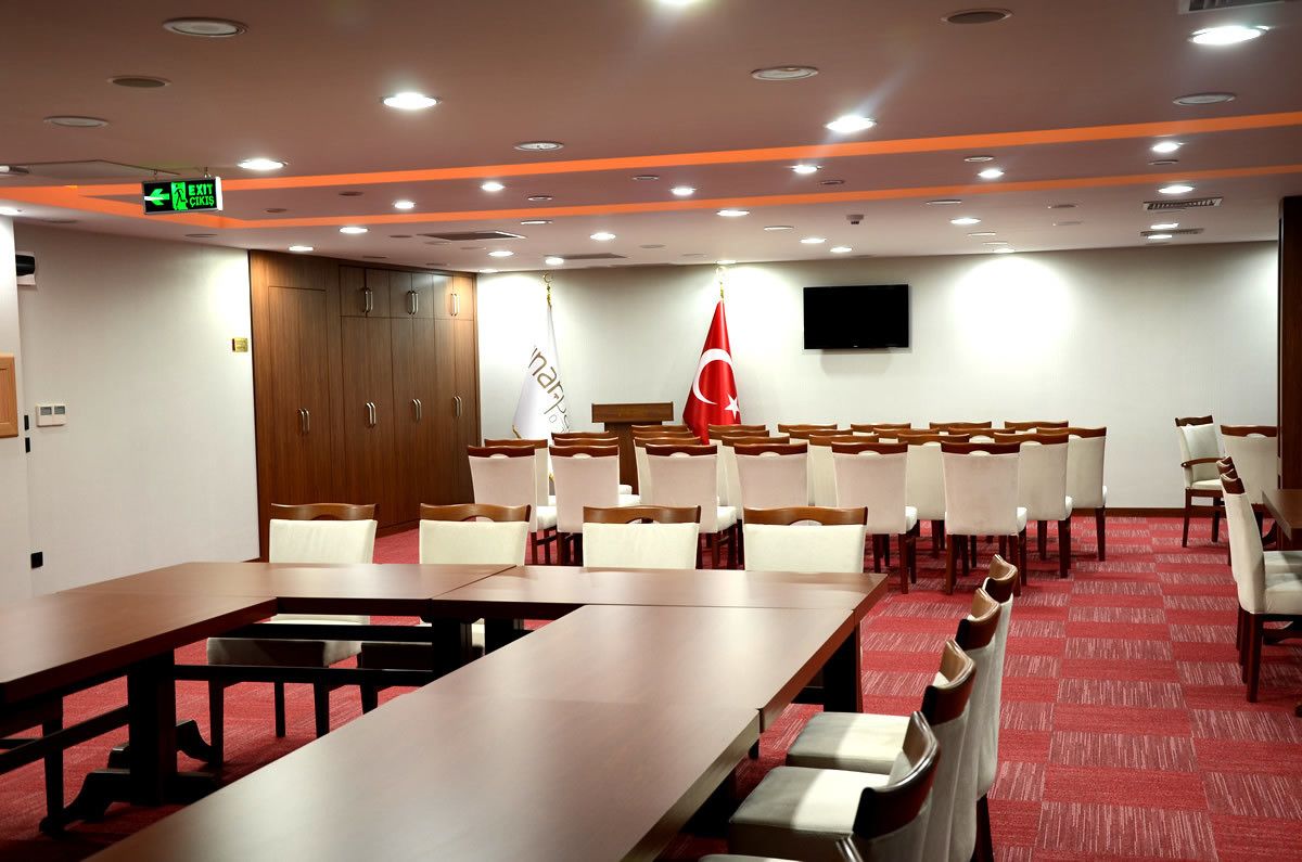 A conference room with a long table, rows of chairs, and flags.