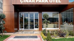 The entrance to the Çinar Park Hotel with a modern facade, glass doors, and a well-maintained garden area. - Cinarpark Hotel (Korfez)