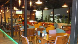 A restaurant with wooden tables and chairs, a bar area, and large windows with a view of parked cars and greenery outside. - Cinarpark Hotel (Korfez)
