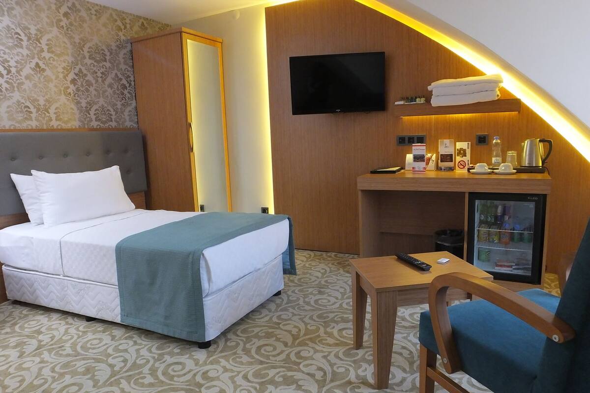 A hotel room with a bed, a desk, a chair, a TV, a minibar, and a refrigerator.