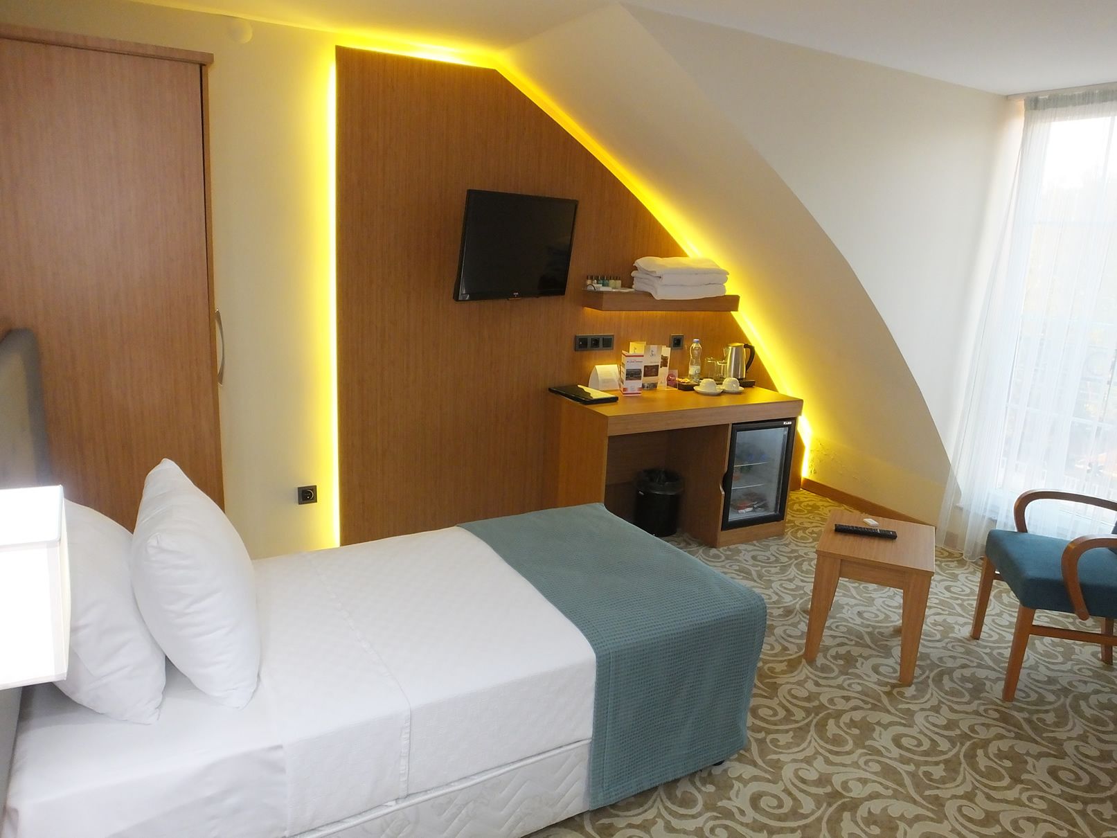 A hotel room with a bed, a desk with a computer, a television, and a small refrigerator.