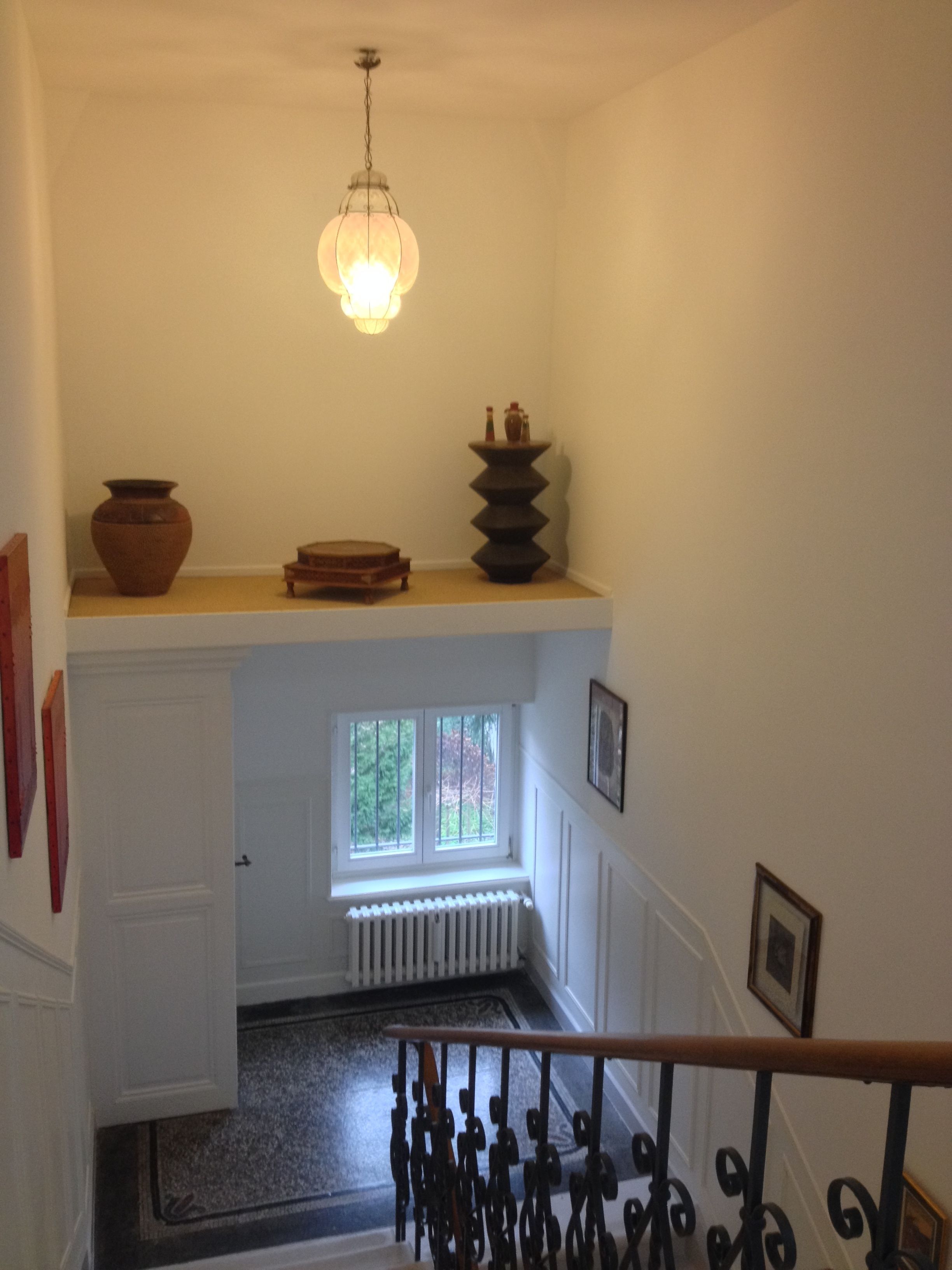 A staircase with a wooden handrail, a radiator below a window, and a hanging light fixture.