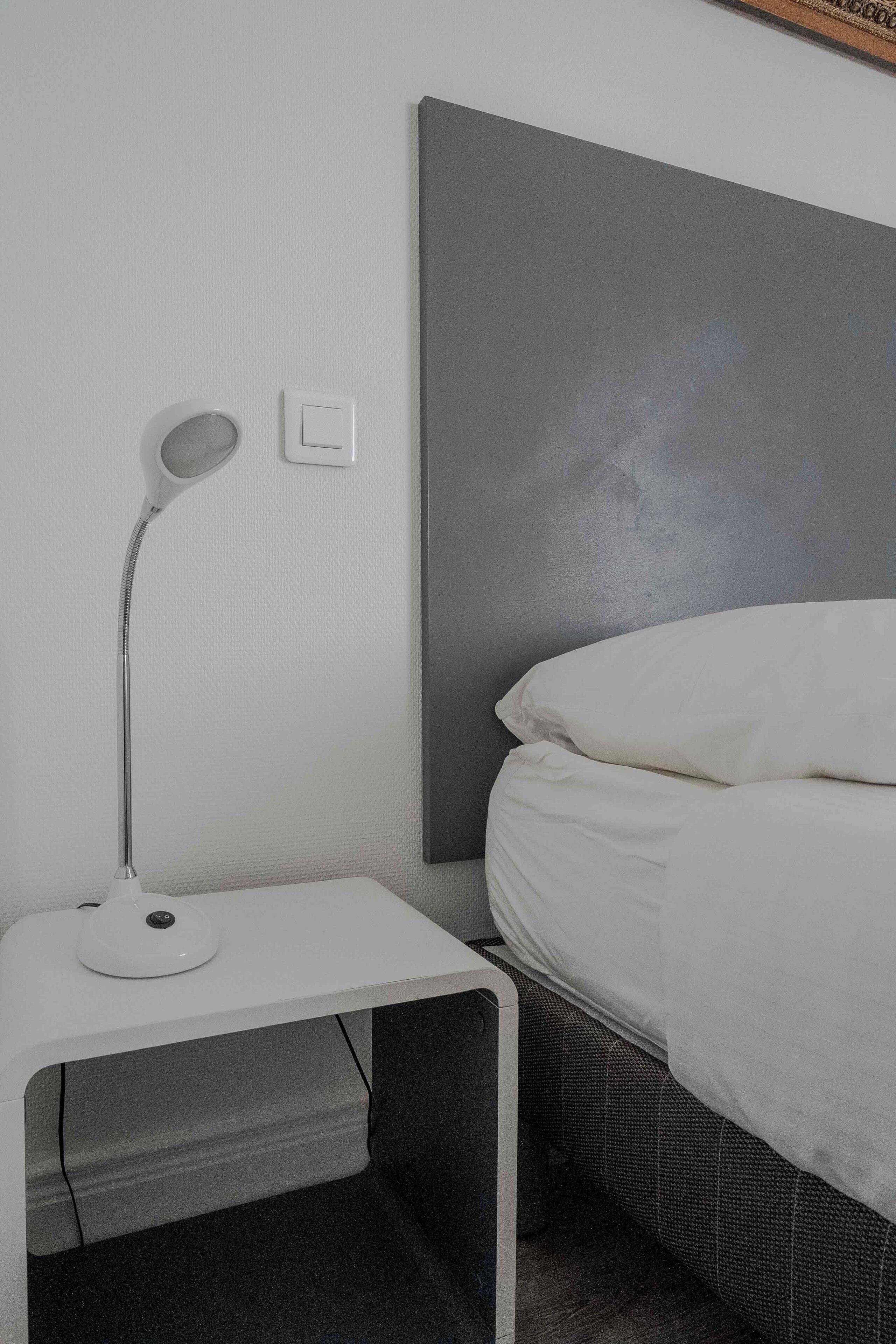 Une chambre à coucher bien rangée, avec un lit, une lampe de chevet et un interrupteur fixé au mur.