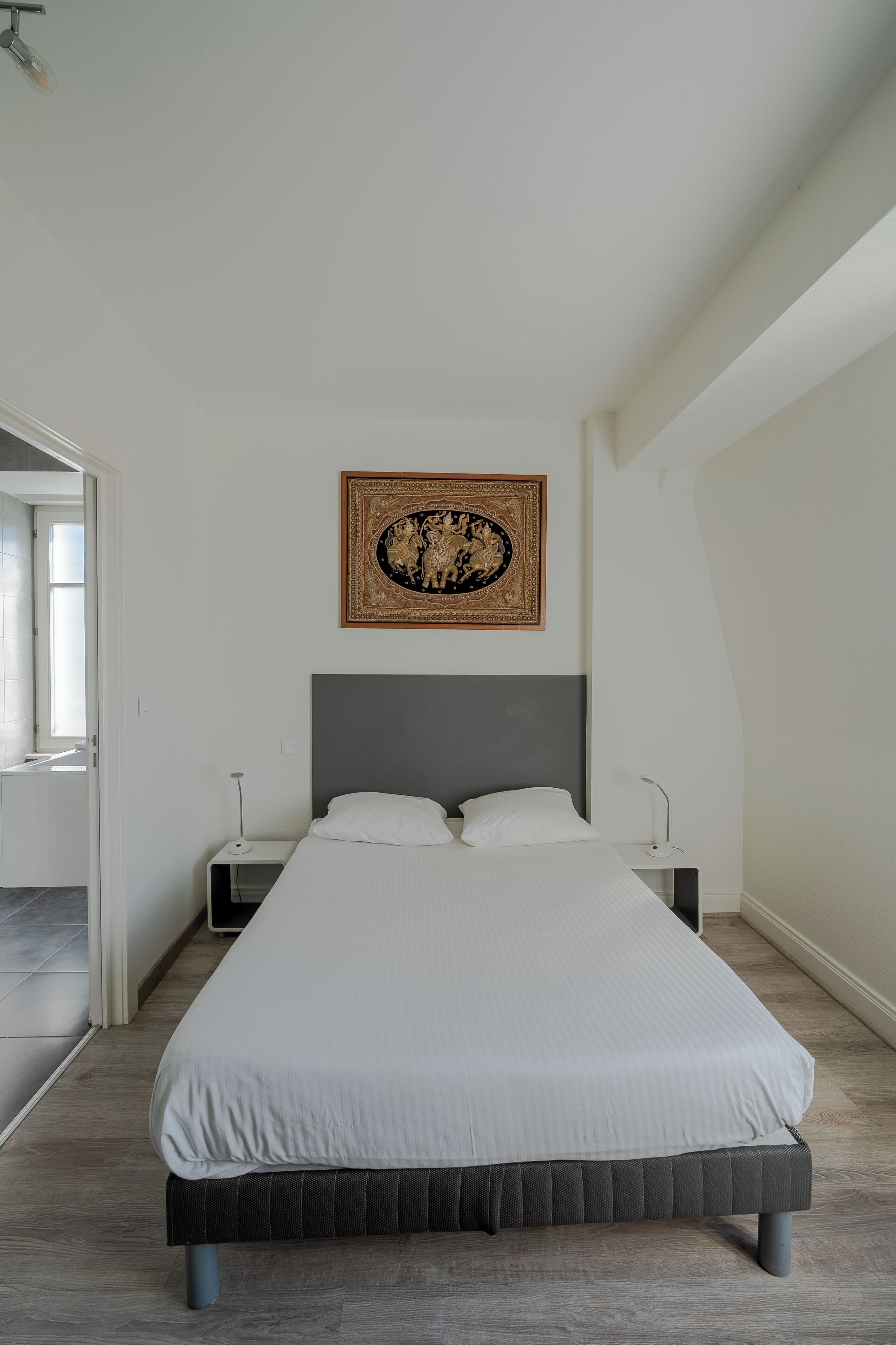 A modern bedroom with a large bed, a headboard, bedside tables, and a wall-mounted artwork.