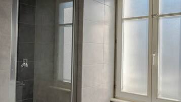 Ein modernes Badezimmer mit einer gläsernen Duschkabine, einem großen Fenster und einem weißen Waschbecken.