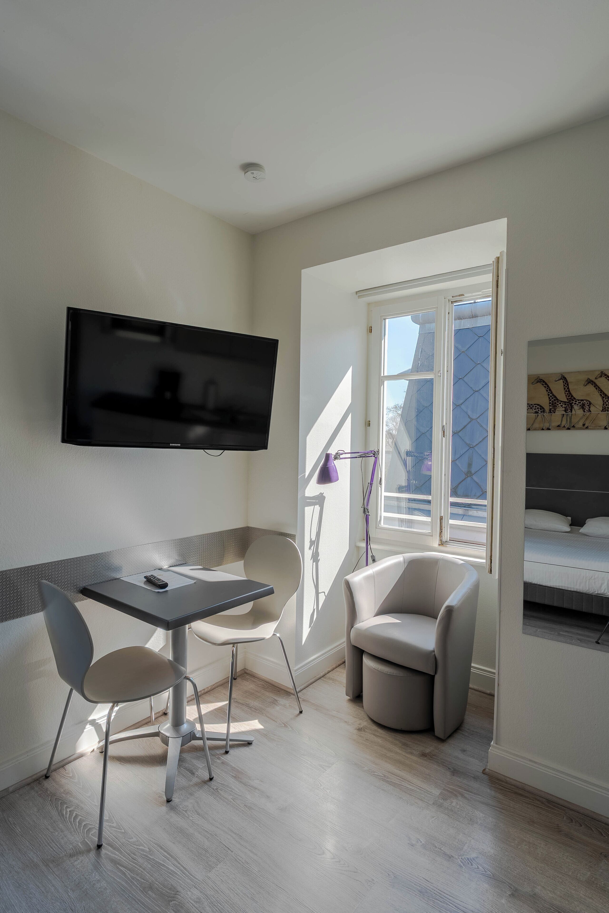 A modern room with a flat-screen TV, a dining table with chairs, a small bathtub, and a window with a view of the outside.