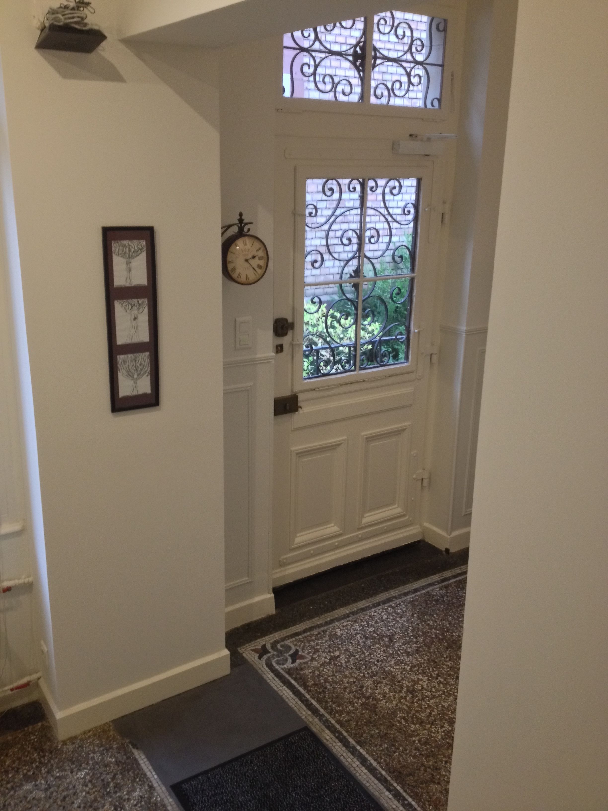 A hallway with a white door, a clock, and a framed picture on the wall.