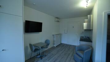 A compact room with a dining table, two chairs, a television, a kitchenette, and a door.