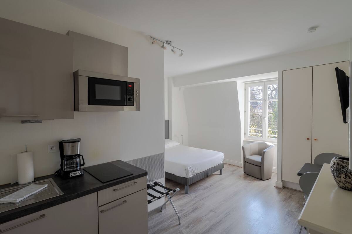 A modern bedroom with a bed, a chair, a desk, a microwave, and a coffee maker.