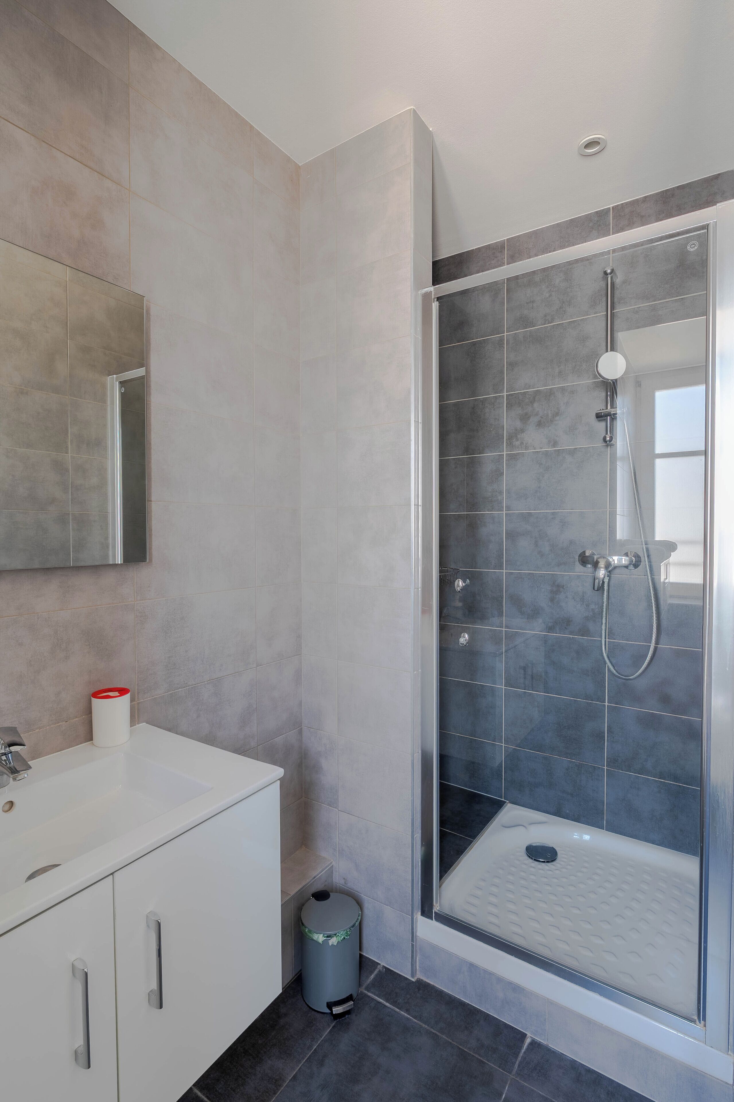 Un baño moderno con ducha de vidrio, un lavabo blanco y un espejo.
