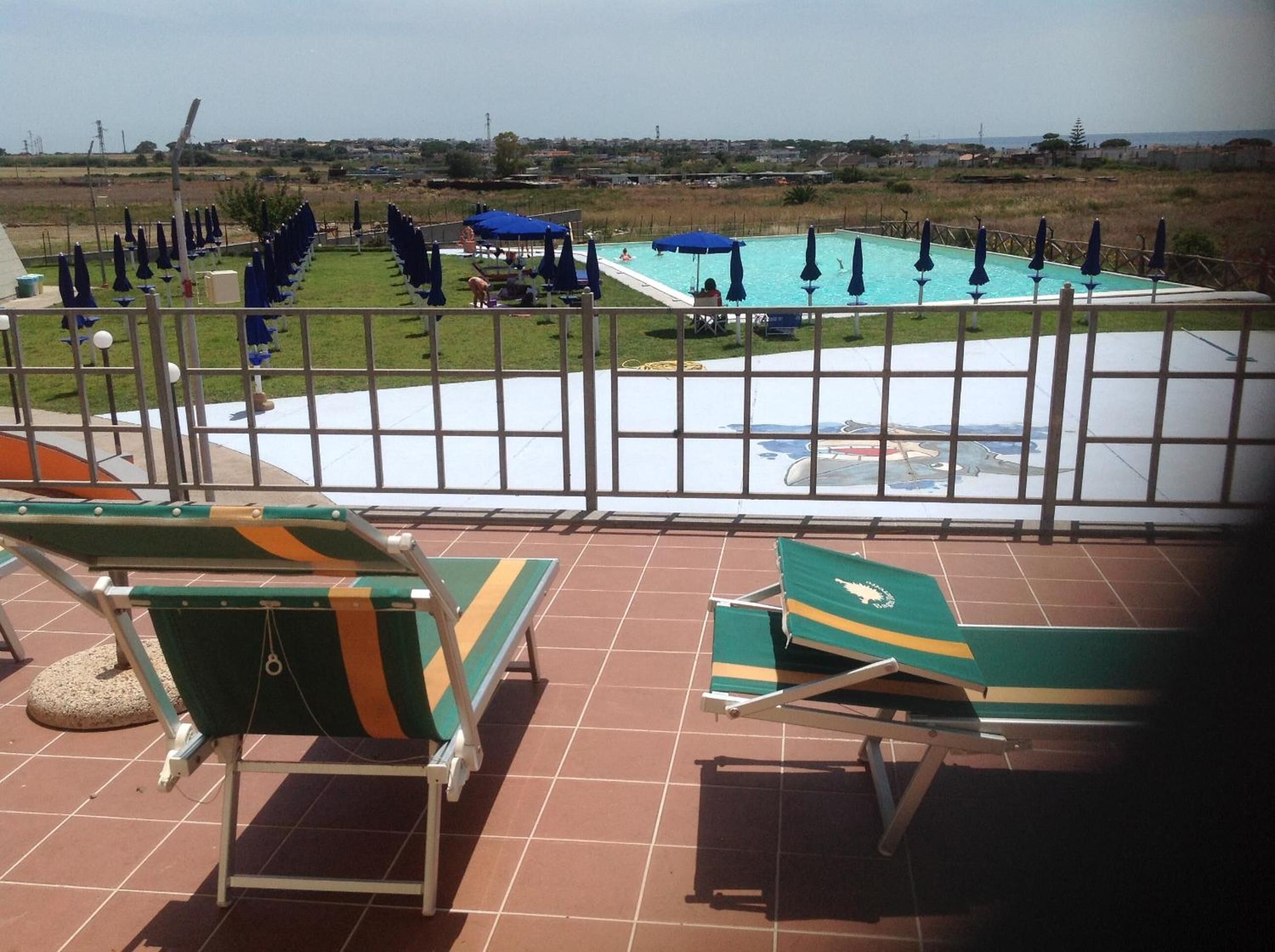 A pool area with lounge chairs and umbrellas, a fenced pool, and a view of the surrounding landscape.
