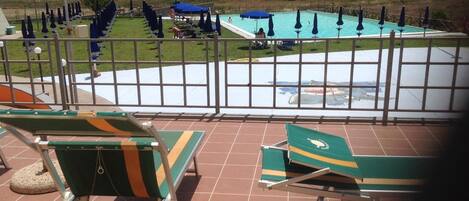 A pool area with lounge chairs and umbrellas, a fenced pool, and a view of the surrounding landscape.