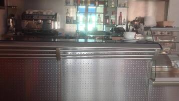 Una cocina industrial con electrodomésticos de acero inoxidable, una máquina de café y estantes con botellas.