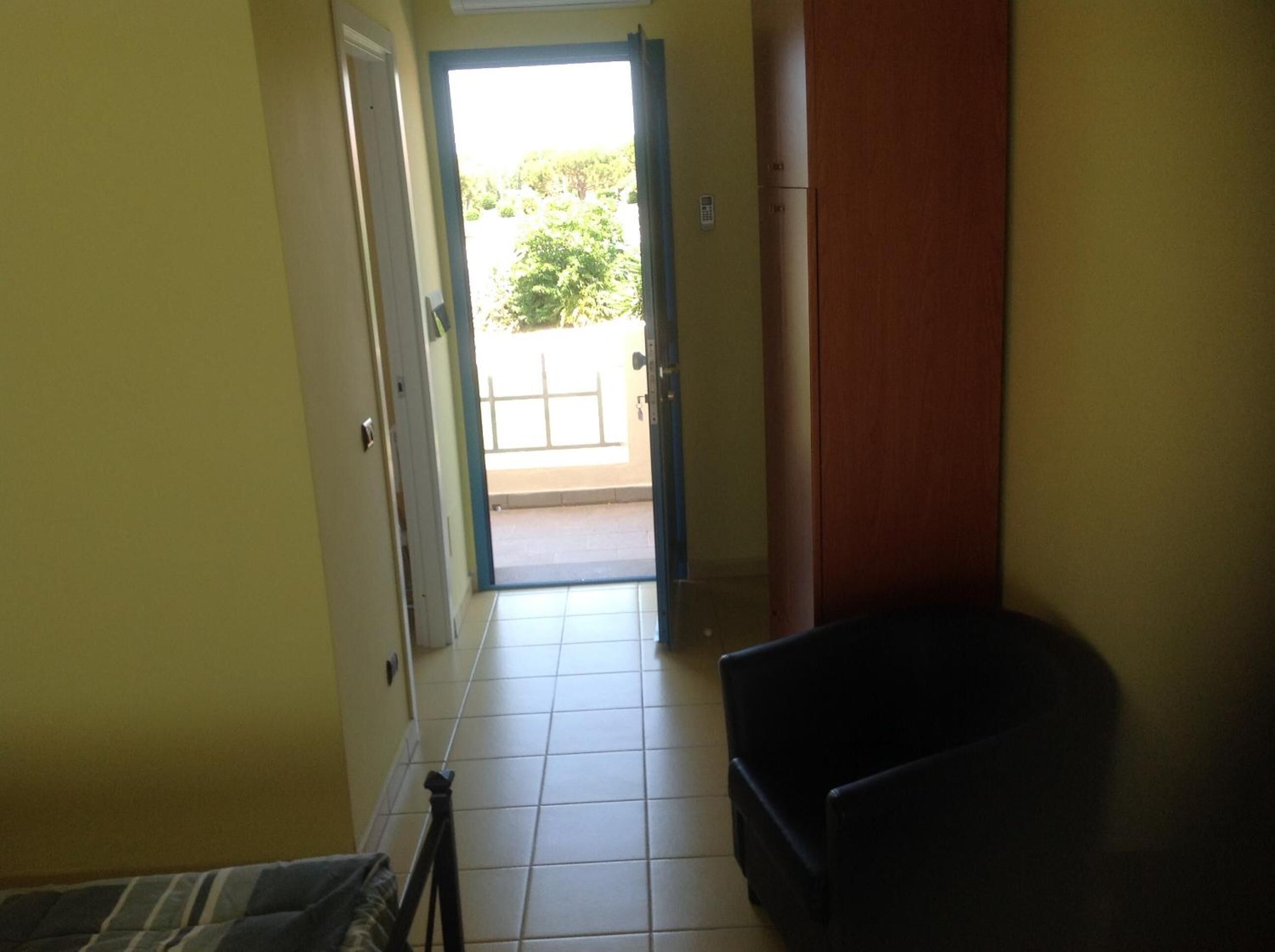 A hallway with a door leading to a balcony, a small table, and a chair.