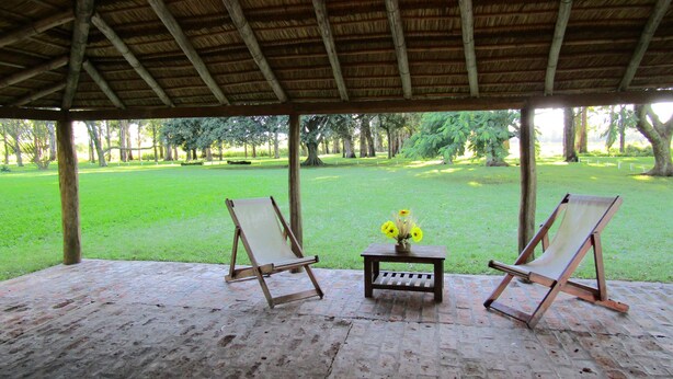 An outdoor covered area with two wooden chairs and a small table with a vase of flowers. - Finca Mombiri (Esquina)