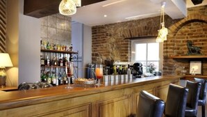 Un espace bar avec un comptoir en bois, des tabourets de bar et un mur en briques. On y trouve des bouteilles et des verres sur le comptoir, ainsi qu’une fenêtre au-dessus du bar.