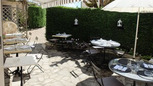 Une terrasse extérieure avec des tables et des chaises, un auvent à rayures et un mur végétal.