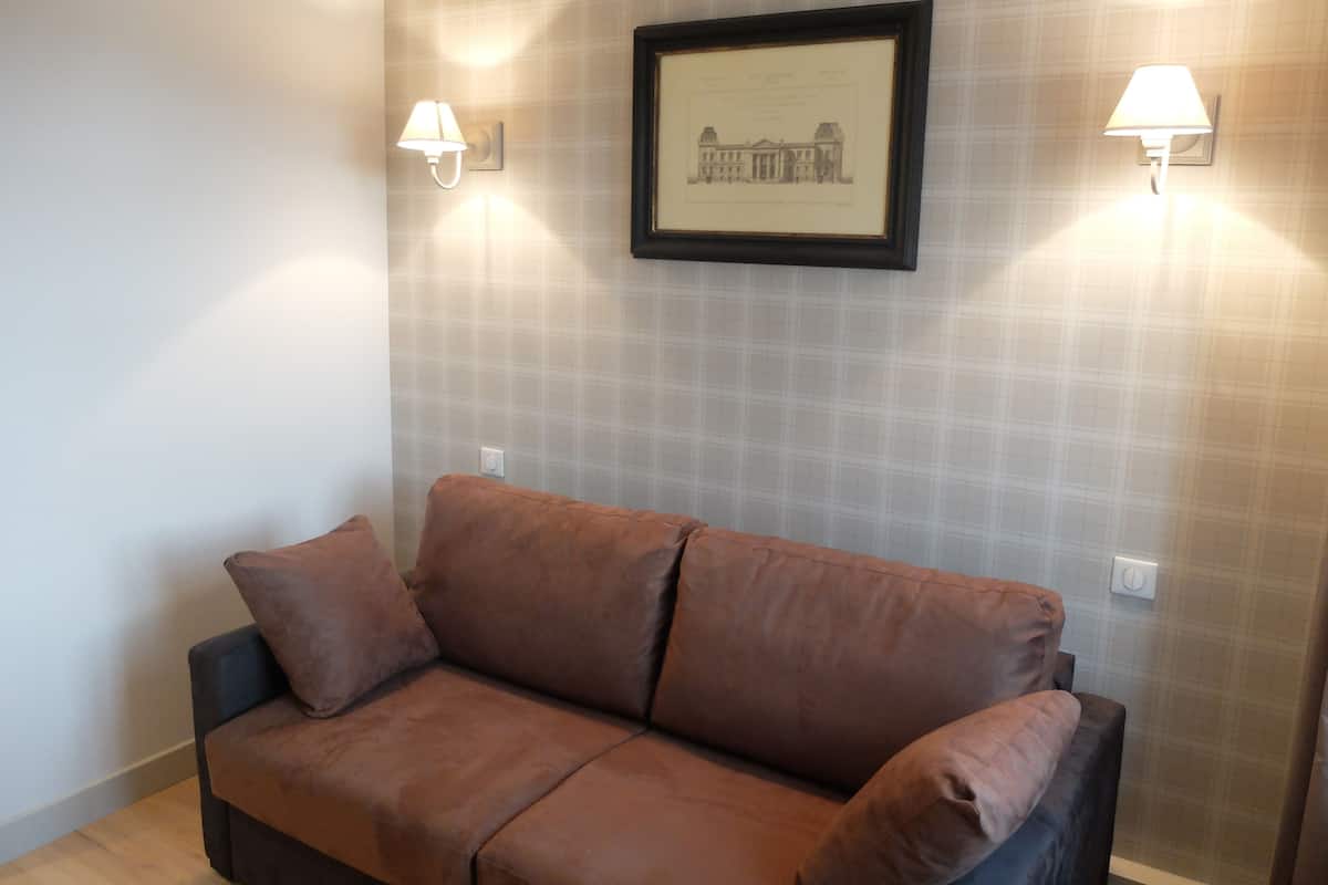 Un sofá marrón en una habitación con papel tapiz escocés y dos lámparas de pared.