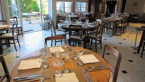 Un restaurant doté de nombreuses tables, aménagé pour accueillir les clients, de grandes fenêtres laissant entrer la lumière naturelle et d’un lustre suspendu au plafond.